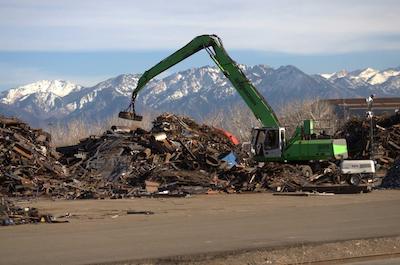 A crane lifting a large pile of scrap metal at a recycling facility.