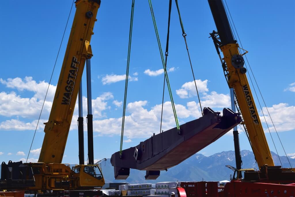 A crane lifting a large object over a field, with workers watching nearby.